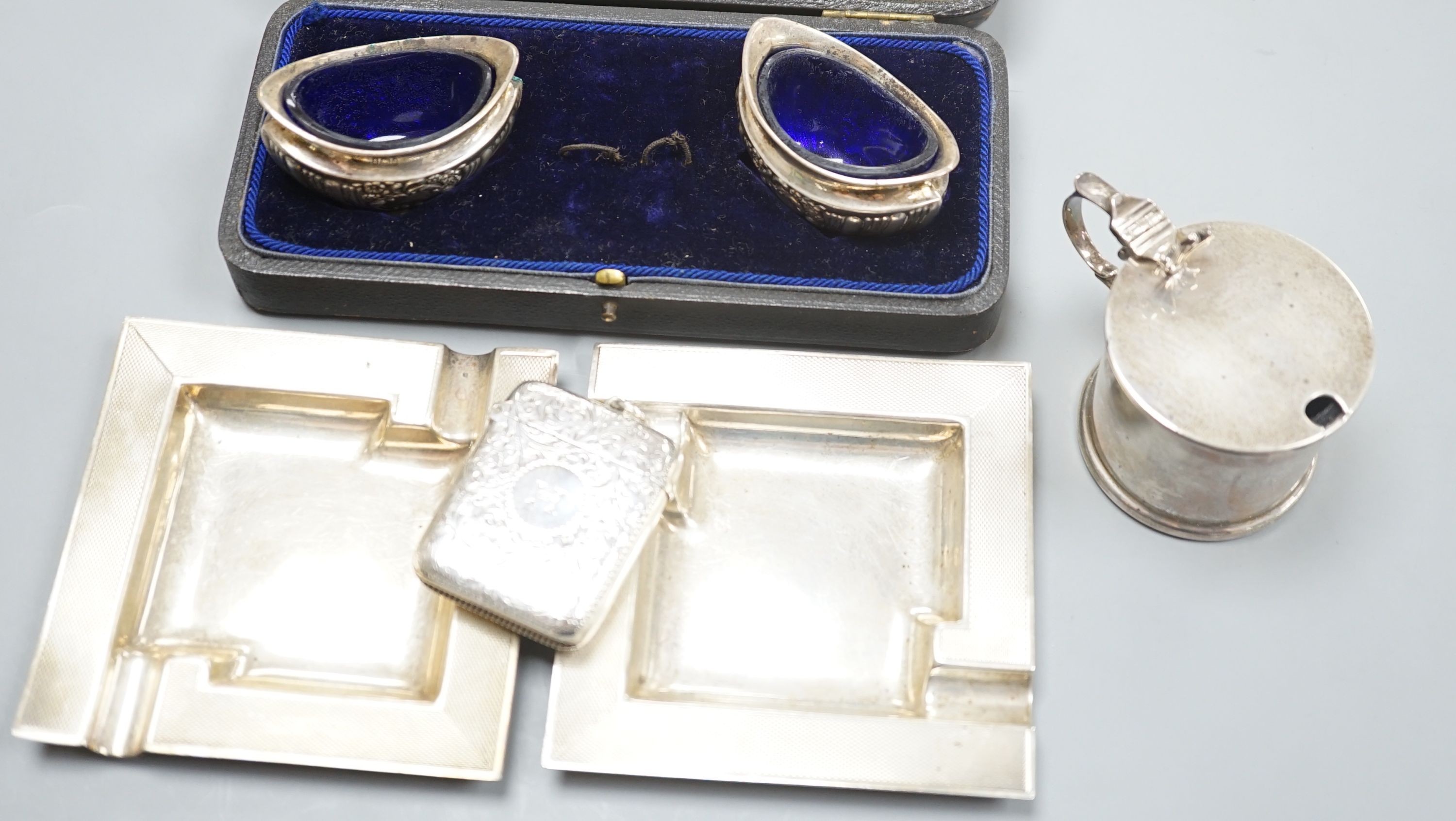 A pair of oval boat shaped salts, with blue glass liners and spoons, cased, Birmingham 1903, no spoons, a Victorian vesta case, all over flat chasing, Birmingham 1888, a pair of square ashtrays, with engine turned border